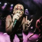 Masked extreme-metal vocalist performing under purple stage lights