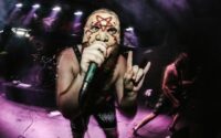 Masked extreme-metal vocalist performing under purple stage lights
